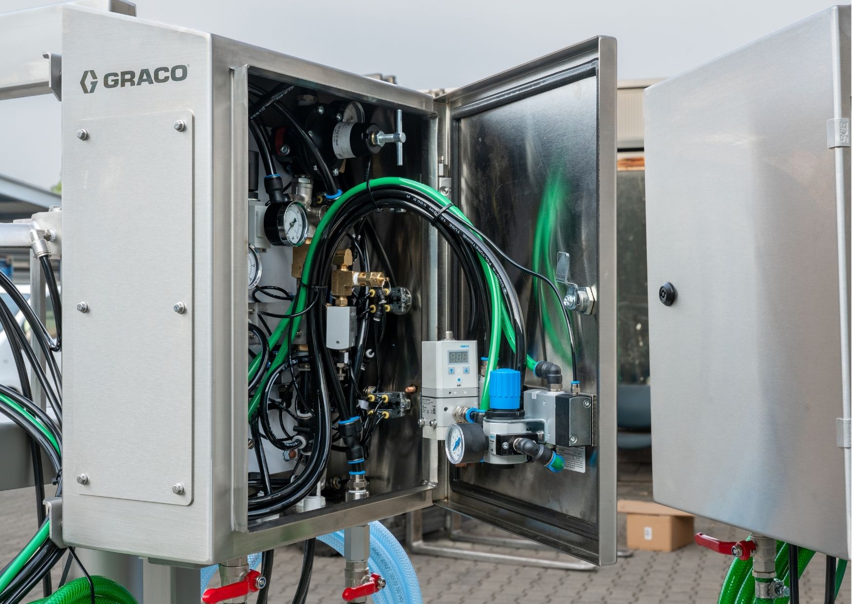 Geopende RVS installatiekast met drukregelaars, manometers en pneumatische leidingen voor een industriële machine.
